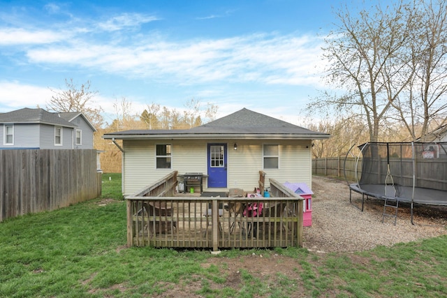rear view of house featuring a deck, a trampoline, fence, and a yard