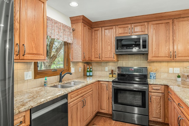 kitchen featuring decorative backsplash, light stone countertops, stainless steel appliances, and a sink