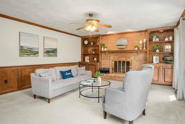 living room featuring ceiling fan, a wainscoted wall, built in features, light colored carpet, and a brick fireplace