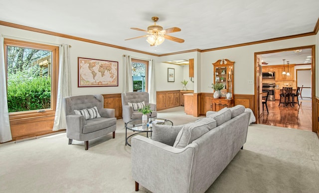 living room with ornamental molding, a ceiling fan, light carpet, and a wainscoted wall