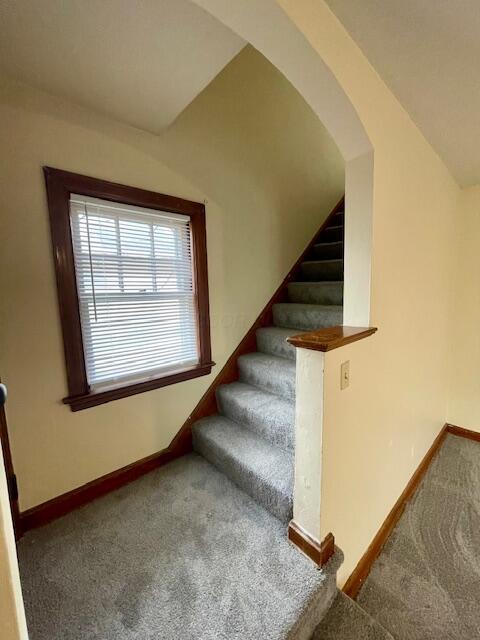 staircase with arched walkways, carpet, and baseboards