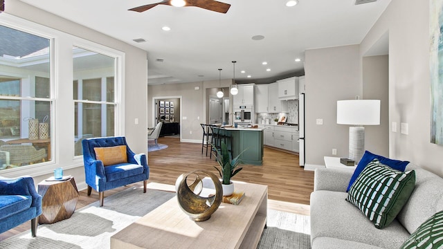 living room featuring recessed lighting, visible vents, a ceiling fan, baseboards, and light wood-style flooring