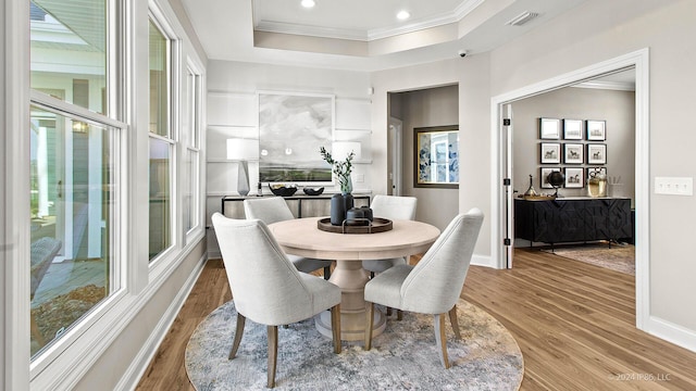 dining space with visible vents, wood finished floors, ornamental molding, and a tray ceiling