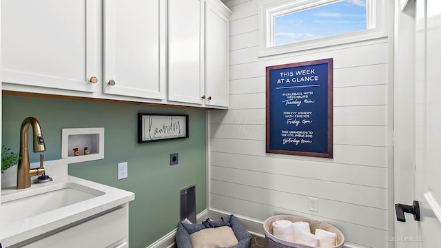 laundry area with a sink, hookup for an electric dryer, washer hookup, wood walls, and cabinet space