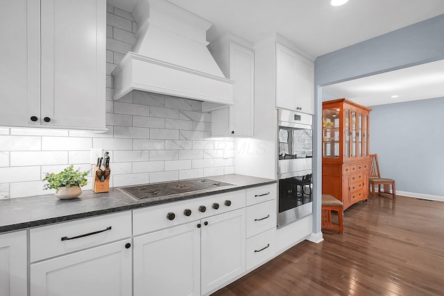 kitchen with custom range hood, cooktop, double oven, and dark countertops