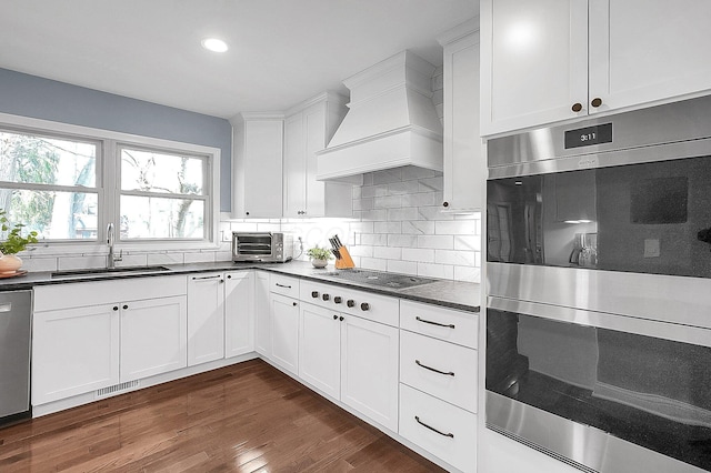 kitchen featuring visible vents, appliances with stainless steel finishes, a sink, dark countertops, and premium range hood