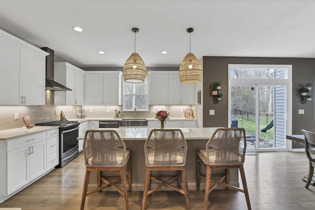 kitchen with stainless steel appliances, wall chimney exhaust hood, decorative backsplash, and wood finished floors