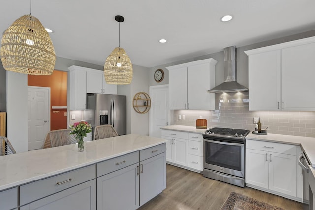 kitchen with wall chimney exhaust hood, light wood-style flooring, appliances with stainless steel finishes, hanging light fixtures, and decorative backsplash
