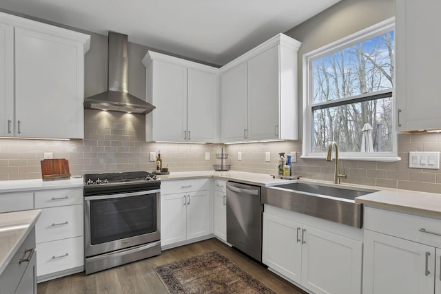 kitchen with a sink, wall chimney range hood, light countertops, dark wood finished floors, and stainless steel appliances