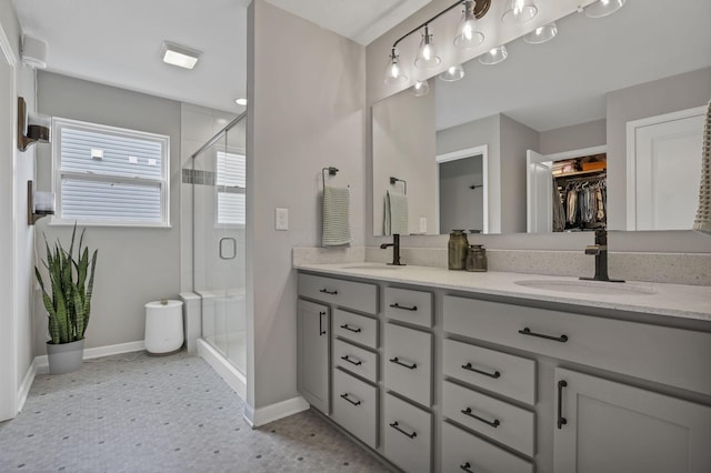 bathroom with a shower stall, double vanity, a sink, and baseboards