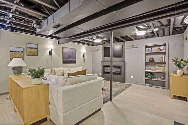 living room with a glass covered fireplace, visible vents, baseboards, and wood finished floors