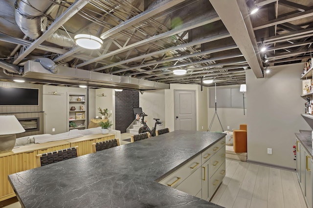 kitchen with a glass covered fireplace, open floor plan, light wood-style floors, and dark countertops