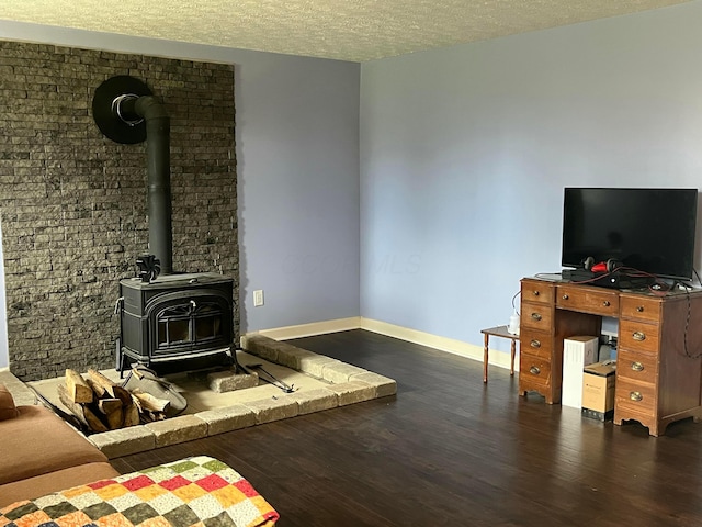 living area with a wood stove, baseboards, wood finished floors, and a textured ceiling