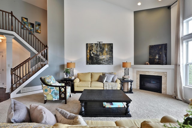 living room featuring a glass covered fireplace, stairs, carpet, and a high ceiling