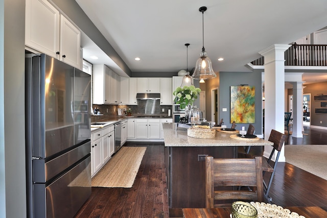 kitchen with decorative columns, a center island, under cabinet range hood, dark wood-type flooring, and stainless steel appliances