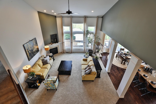 living room with a towering ceiling, a fireplace, recessed lighting, ceiling fan, and wood finished floors