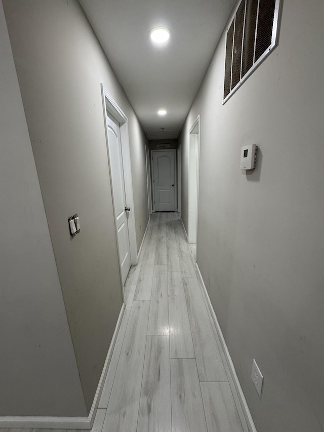 corridor featuring baseboards, visible vents, and light wood finished floors