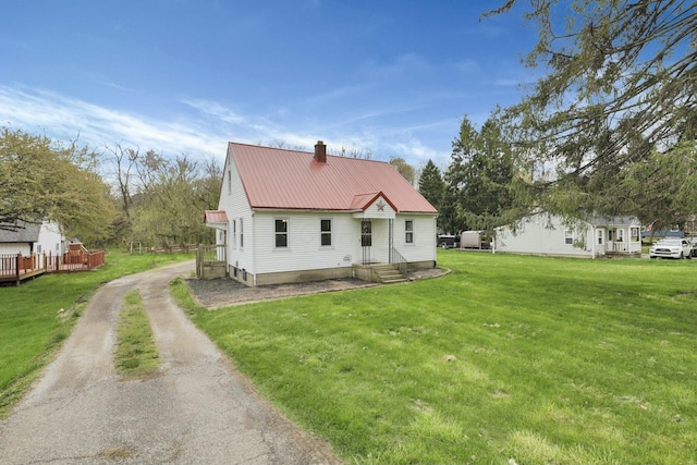 back of house featuring a chimney, metal roof, driveway, and a lawn