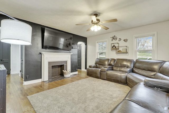 living area with a fireplace with flush hearth, wood finished floors, a ceiling fan, and a healthy amount of sunlight
