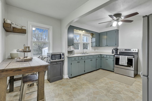 kitchen featuring a sink, light countertops, appliances with stainless steel finishes, stone finish floor, and a ceiling fan