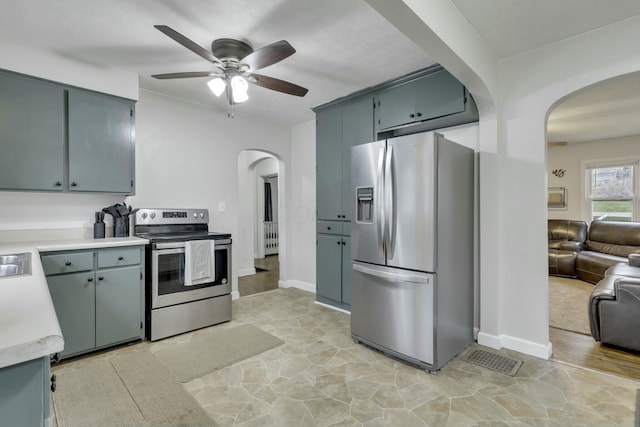kitchen featuring baseboards, arched walkways, light countertops, a ceiling fan, and stainless steel appliances