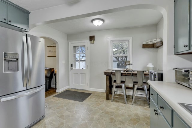 kitchen featuring arched walkways, stone finish floor, gray cabinets, appliances with stainless steel finishes, and light countertops