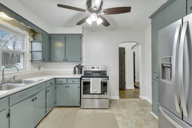 kitchen with a ceiling fan, open shelves, stainless steel appliances, arched walkways, and a sink