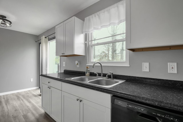 kitchen with dishwasher, a sink, light wood-type flooring, dark countertops, and white cabinetry