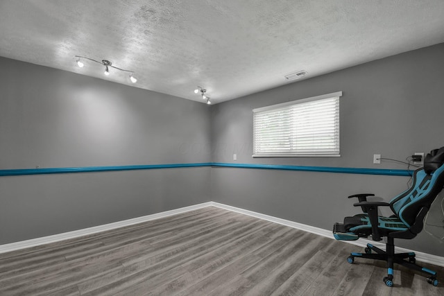 unfurnished office featuring baseboards, rail lighting, a textured ceiling, visible vents, and wood finished floors