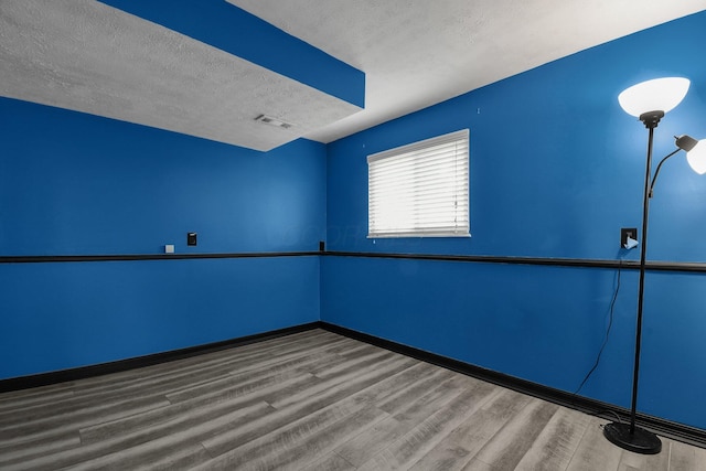 spare room with visible vents, baseboards, wood finished floors, and a textured ceiling