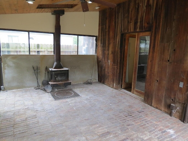 11 Plumb St, Lockbourne, OH 43137 - unfurnished living room featuring a wood stove, ceiling fan, wooden ceiling, brick floor, and wooden walls