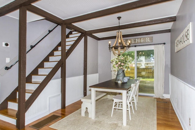 dining area featuring an inviting chandelier, a wainscoted wall, stairway, wood finished floors, and beam ceiling