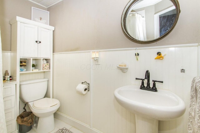 full bath with tile patterned flooring, wainscoting, a sink, and toilet