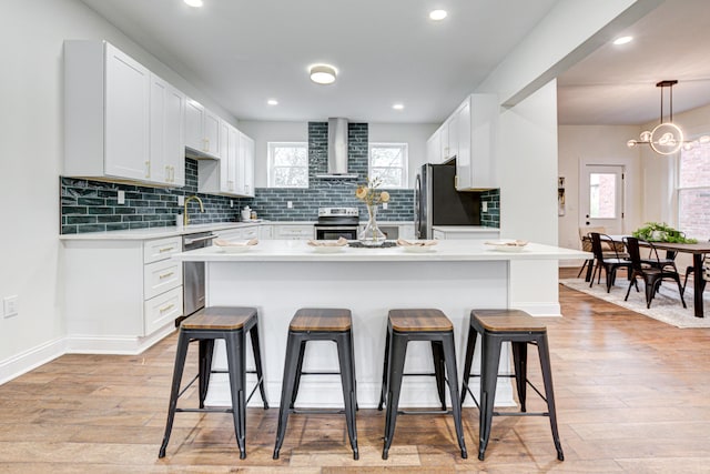 344 E Whittier St, Columbus, OH 43206 - kitchen featuring a breakfast bar area, stainless steel appliances, light wood-style floors, light countertops, and wall chimney range hood