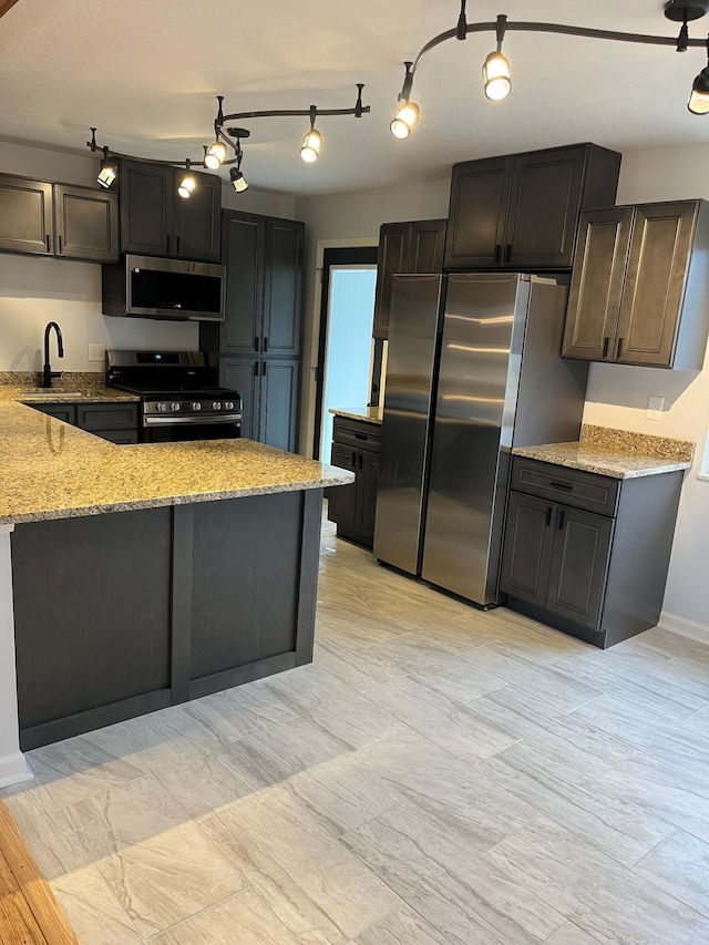 kitchen featuring a peninsula, appliances with stainless steel finishes, light stone counters, a sink, and baseboards