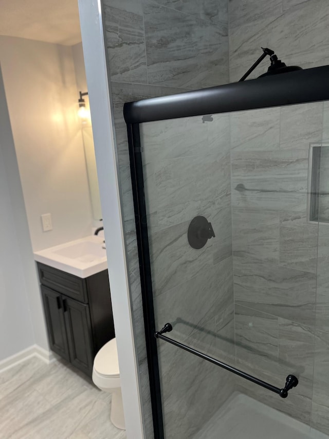bathroom with a shower stall, vanity, baseboards, and toilet