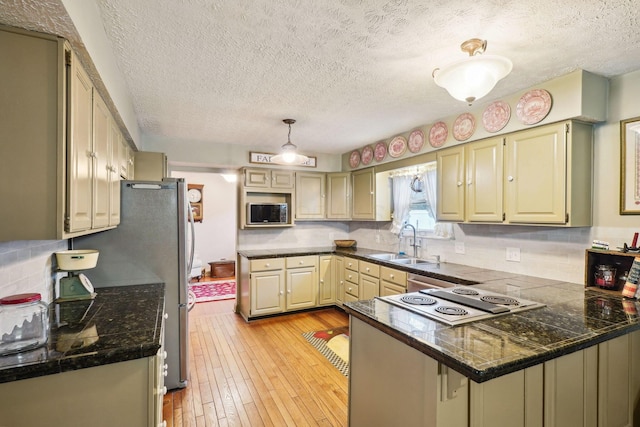 kitchen with tasteful backsplash, a peninsula, a sink, stainless steel appliances, and light wood finished floors