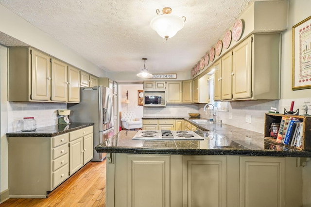kitchen with light wood-style floors, a peninsula, a sink, stainless steel appliances, and backsplash