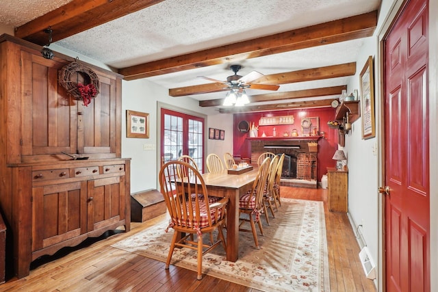 dining area featuring light wood-type flooring, ceiling fan, a fireplace, and beam ceiling