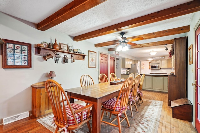 dining space with visible vents, baseboards, ceiling fan, light wood-type flooring, and beam ceiling