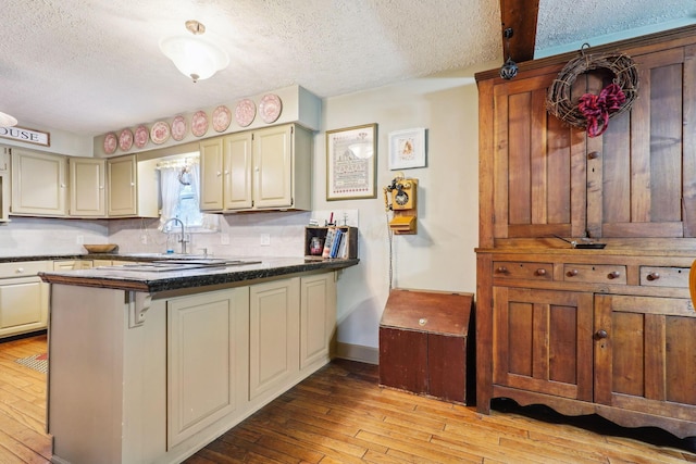 kitchen with a peninsula, light wood-style flooring, a textured ceiling, backsplash, and dark countertops