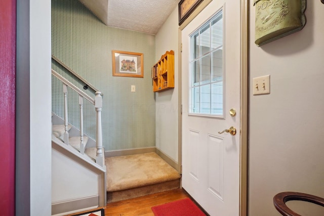 doorway with a textured ceiling, wood finished floors, baseboards, and stairs