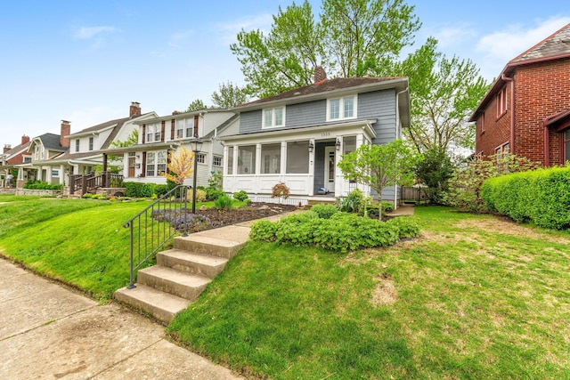 american foursquare style home featuring a chimney, a front lawn, and a sunroom