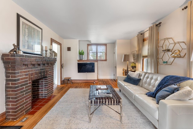 living area featuring baseboards, wood finished floors, and a brick fireplace