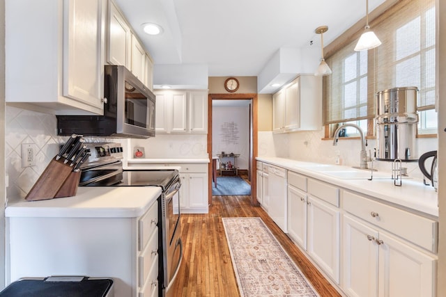 kitchen featuring wood finished floors, decorative backsplash, stainless steel appliances, white cabinets, and a sink