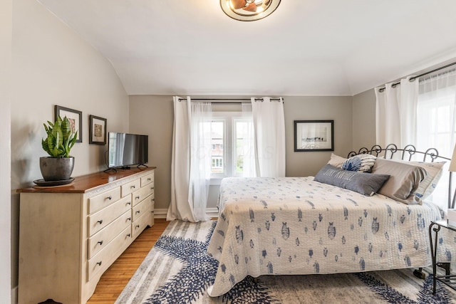 bedroom with baseboards, multiple windows, light wood-style flooring, and vaulted ceiling
