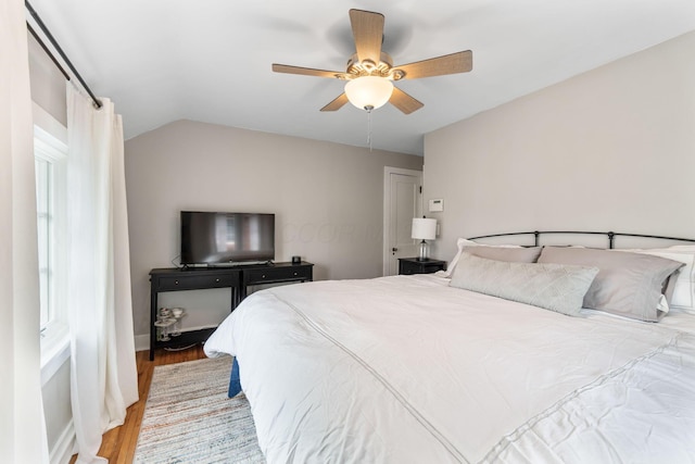 bedroom with a ceiling fan, vaulted ceiling, wood finished floors, and baseboards
