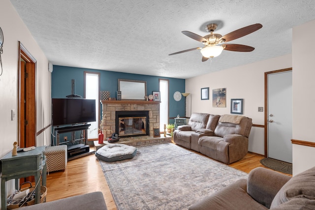 living room with a ceiling fan, a textured ceiling, a fireplace, and light wood-style flooring