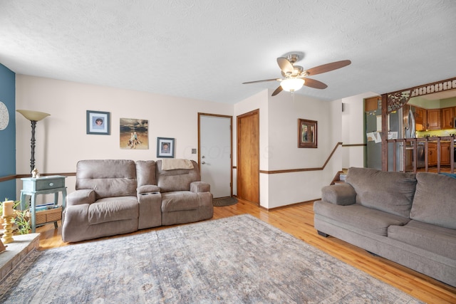 living room featuring a textured ceiling, ceiling fan, light wood-style flooring, and baseboards