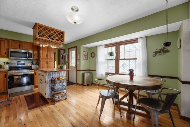 kitchen featuring a textured ceiling, appliances with stainless steel finishes, light wood finished floors, and brown cabinets